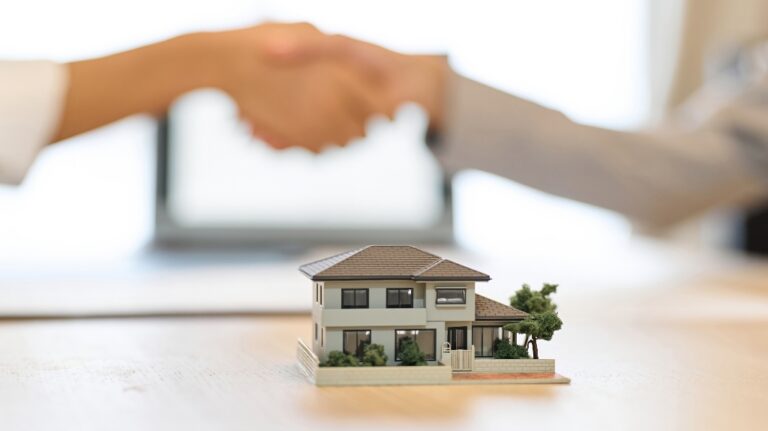 woman and a man shake hands next to a toy model of a house