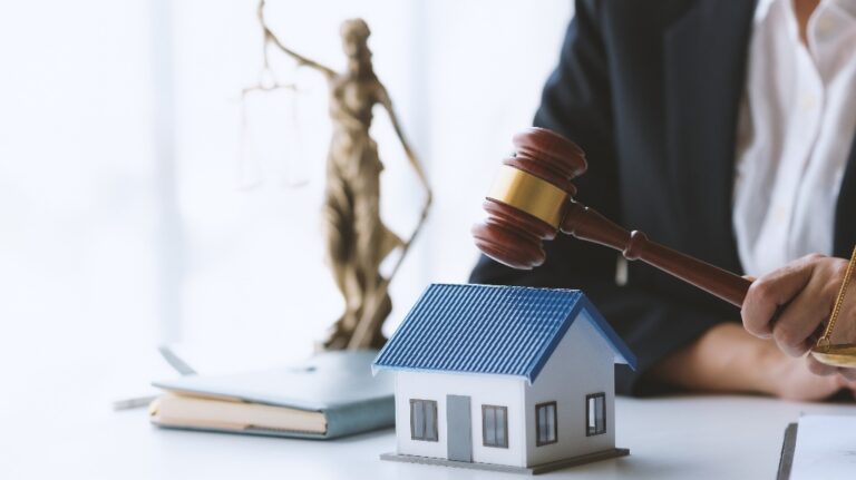 Lawyer holding gavel near model house and justice scale