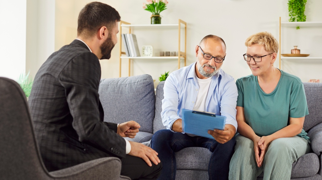 Smiling elderly couple meets agent at home, reviewing documents